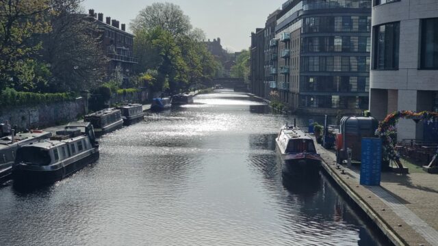 Early morning sun reflects in the water of a peaceful wide canal in central London.